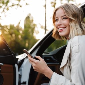 Image of young caucasian beautiful businesslike woman sitting in luxury car and using cellphone